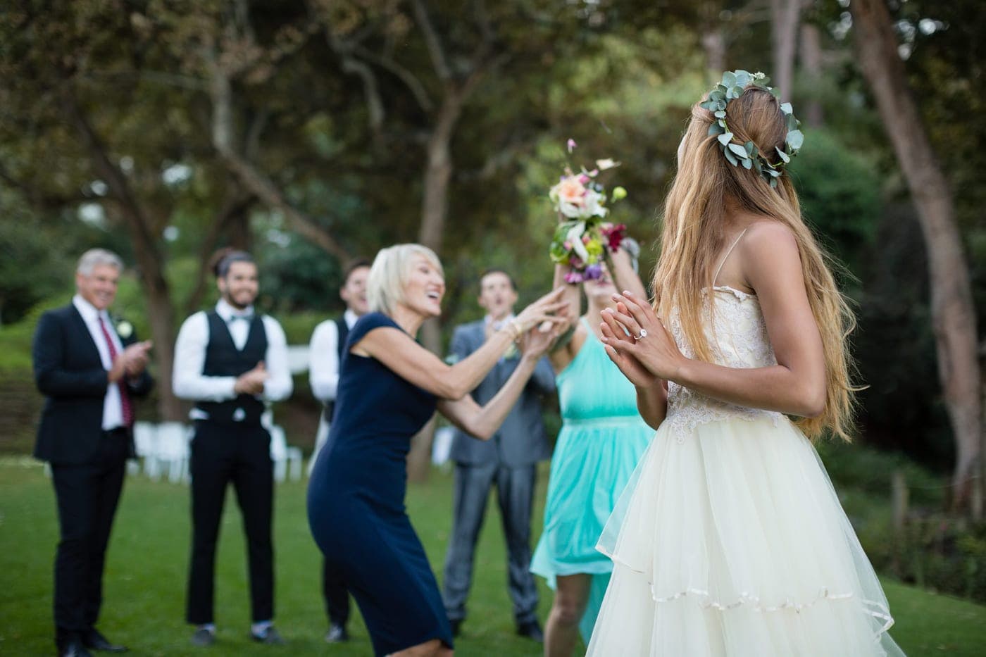 Braut wirft den Brautstrauss rückwärts zu einer Gruppe wartender Gäste im Garten, ein traditioneller Moment der Unterhaltung auf jeder Hochzeit.