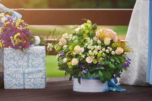 Blumenarrangement neben verpackten Hochzeitsgeschenken auf Holzterrasse