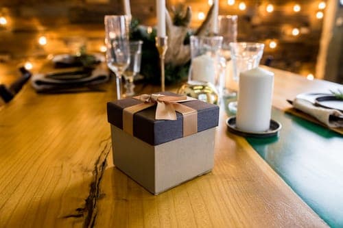 Stilvoll verpacktes Gastgeschenk zur Hochzeit mit goldener Schleife auf einem Holztisch als persönliches Dankeschön und Teil der Tischdeko