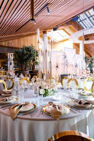 Round tables laid with gold charger plates, tall candelabras and pale pink flowers, decorated for a golden wedding anniversary