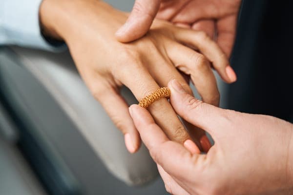 Ein breiter, goldener Ring mit einzigartiger Spiralstruktur wird an den Ringfinger einer Frau gesteckt.