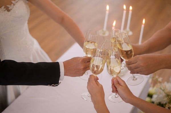 Mehrere Hände stossen mit Champagnergläsern an, Brautkleid im Bild; ein passender Moment für Glückwünsche zur Hochzeit beim Apéro.