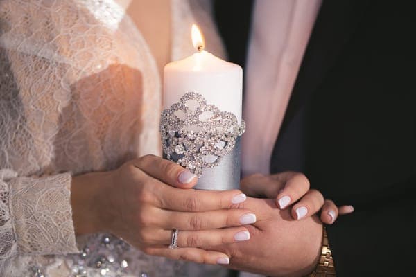 Brautpaarhände halten eine brennende Hochzeitskerze