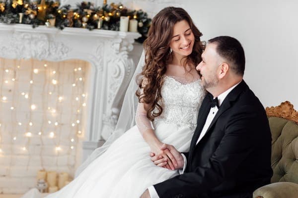 Junges verliebtes Paar, Braut und Bräutigam posieren im Studio vor einem mit einem Weihnachtsbaum geschmückten Hintergrund an ihrem Hochzeitstag zu Weihnachten. Geniessen Sie einen Moment des Glücks und der Liebe für die diamantene hochzeit
