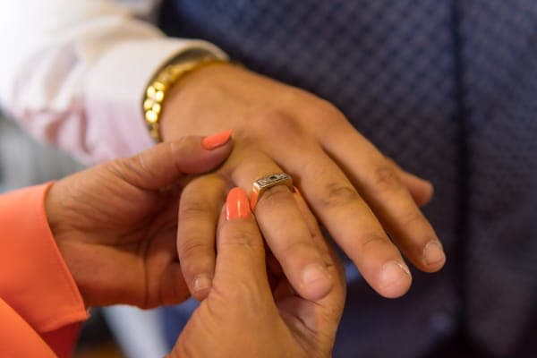 A woman's hands slipping a gold signet-style ring onto a man's finger