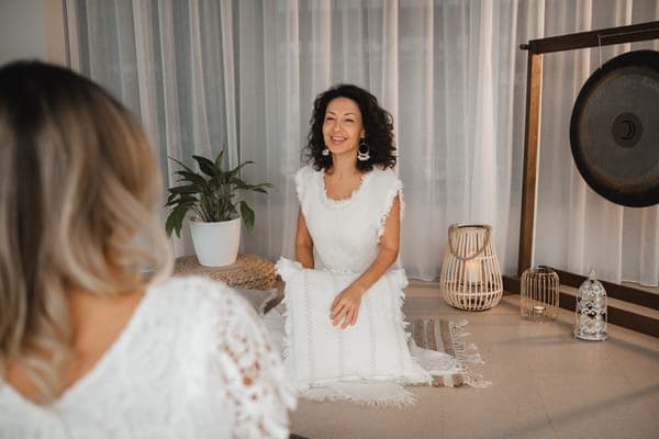 Lächelnde Frau in Weiss bei einer Klangmeditation mit Gong im Hintergrund.