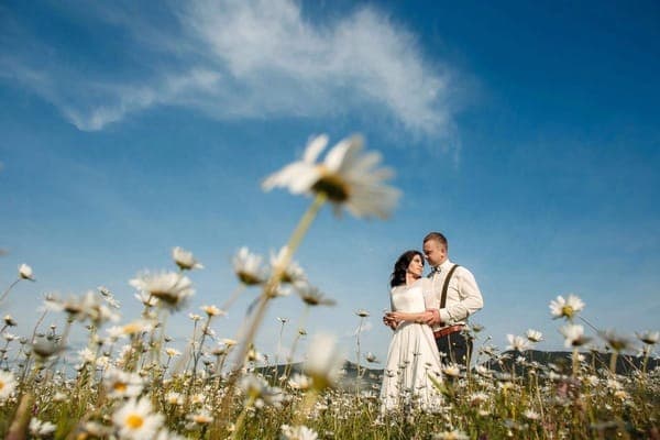 Ein frisch vermähltes Paar in einer Blumenwiese, ein Symbol für die junge Liebe, die über Jahrzehnte zur unzerbrechlichen Stärke einer Eisernen Hochzeit heranreift.