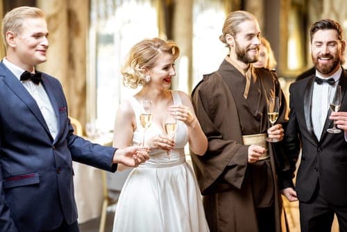Braut im weissen Kleid und drei Männer im Anzug, darunter ein Mann im braunen Gewand, stehen zusammen.