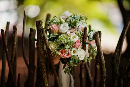 Brautstrauss aus rosa und weissen Rosen steckt zwischen rustikalen Holzstangen; grüner Hintergrund ist weich verschwommen.