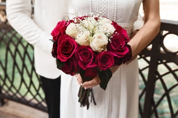 Braut und Bräutigam halten einen Brautstrauss aus roten und weissen Rosen.