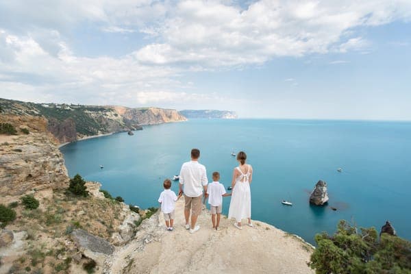 Une famille en vêtements clairs debout sur une falaise, le regard tourné vers la mer