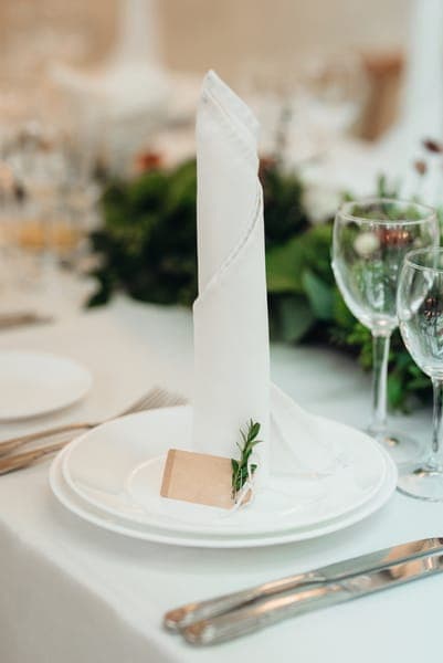 Elegant gedeckter Hochzeitstisch mit aufrecht gefalteter weisser Serviette, Namenskärtchen und Weingläsern.