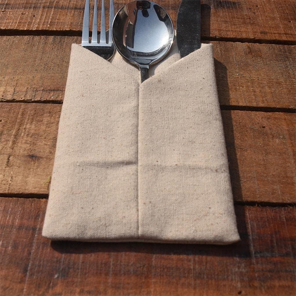 Beige Stoffserviette als Bestecktasche gefaltet, mit Messer, Gabel und Löffel auf Holztisch.