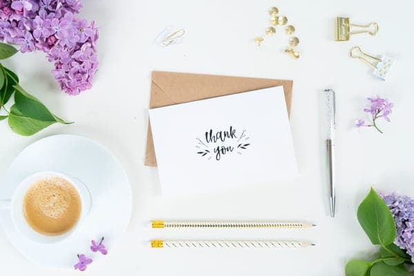 Flatlay mit „Thank you“-Karte auf Umschlag, Flieder, Espresso und Stift
