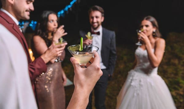 Friends raising cocktail glasses at an evening party outdoors, with a bride in a white gown among them