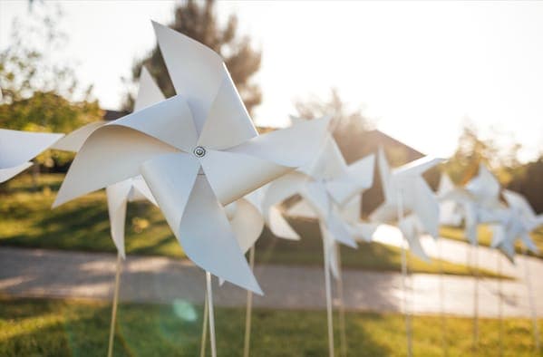 Weisse Windräder als Hochzeitsdeko im Garten, im warmen Gegenlicht der Abendsonne entlang eines Weges aufgestellt.