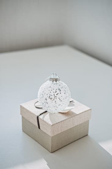 Weisse Glaskugel mit Glitzer liegt auf einer beigefarbenen Geschenkbox mit Band auf einem hellen Tisch