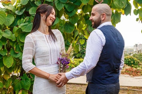 Brautpaar hält Hände im Garten – petersilienhochzeit mit Kräuterstrauss draußen