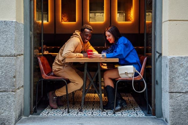 Zwei Freunde sitzen im gemütlichen Café und lachen, während sie gemeinsam auf ein rotes Smartphone schauen.