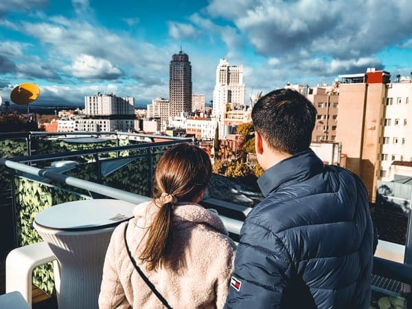 Ein Paar steht auf einem Rooftop und blickt über eine Stadt mit Hochhäusern unter dramatischen Wolken.