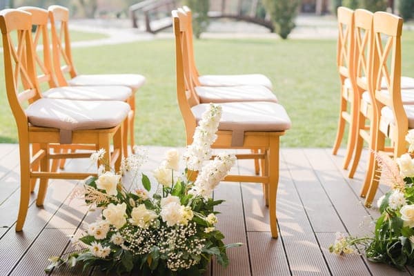 Detailansicht einer eleganten Sitzordnung für die Hochzeit, bei der Holzstühle mit Blumenschmuck den Weg zum Altar säumen.