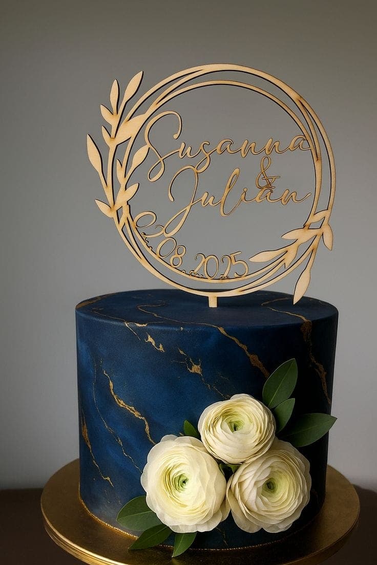 Ein eleganter Cake Topper Hochzeit personalisiert in Gold, der mit Namen und einem Kranz eine dunkelblaue Hochzeitstorte verziert.
