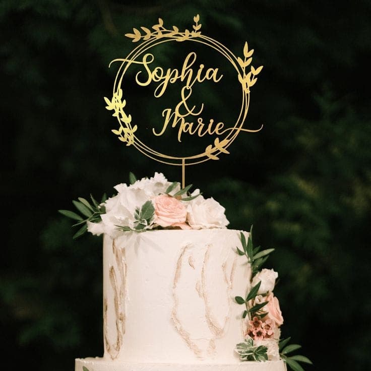 Ein filigraner, goldener Cake Topper Hochzeit personalisiert mit den Namen „Sophia & Marie“ in einem Blätterkranz auf einem eleganten Hochzeit Cake.