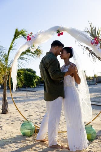 Eng umschlungenes Paar unter einem Traubogen am Strand, feiert ihre intime Strandhochzeit.