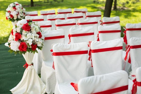 Festlich dekorierte Stühle mit roten Schleifen, die die Sitzordnung der Hochzeit für die Trauungszeremonie im Freien bilden.