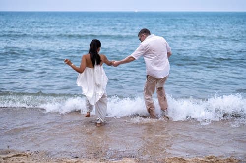 Frisch vermähltes Paar tanzt oder spaziert nach ihrer Strandhochzeit ins Meer.