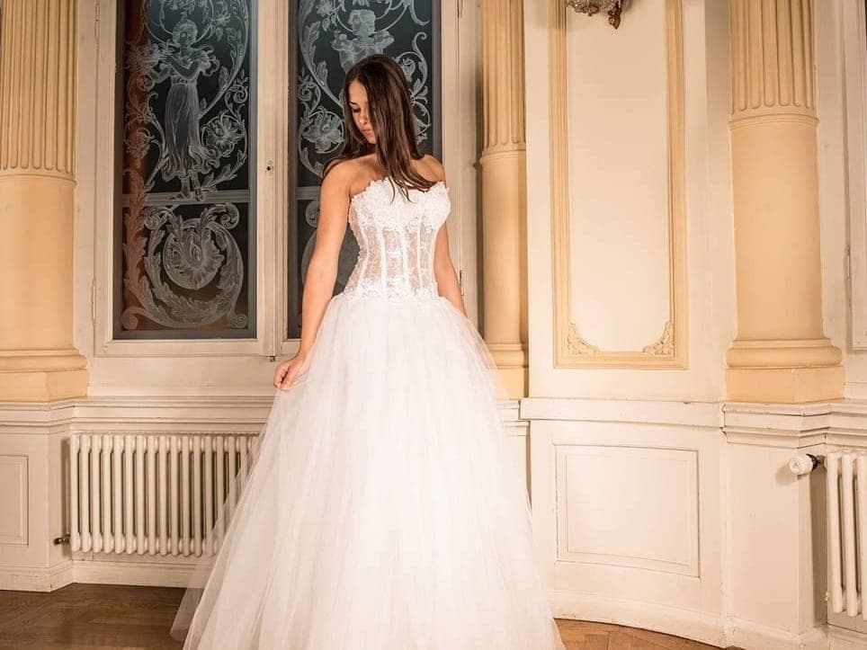 Frau in einem weissen Brautkleid mit Spitzenkorsage und weitem Tüllrock in einem Saal mit Säulen