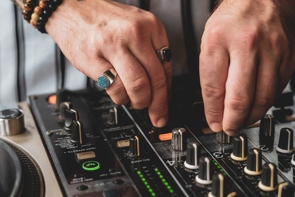Zwei Hände mit Ringen und Armbändern drehen an den Reglern eines DJ-Mischpults