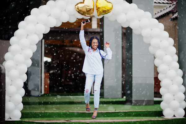 Jubelnde Frau läuft durch weissen Ballonbogen mit goldenen Herzen.