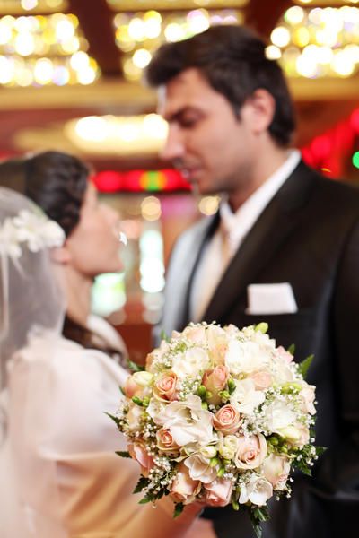 Persönliche Glückwünsche zur Hochzeit: So findest du die perfekten Worte Hochzeitswünsche, Hochzeitsblog Detaillierter Brautstrauss mit pastellfarbenen Rosen im Vordergrund, dahinter steht das Brautpaar unscharf im romantischen Licht.