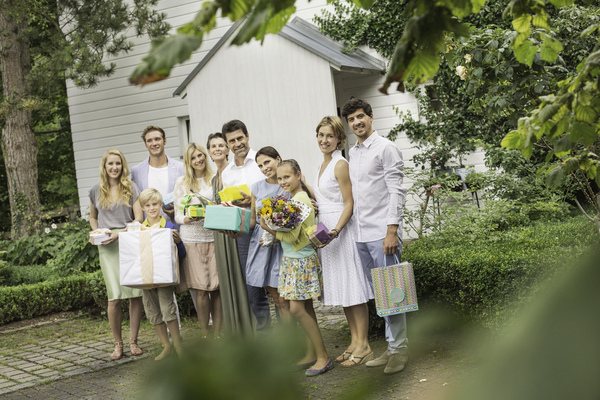 Hochzeitsgäste stehen mit verpackten Geschenken und Blumen fröhlich vor dem Haus.