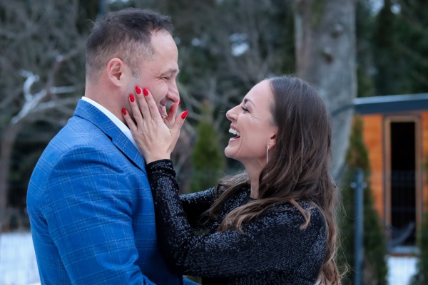 Heiratsantrag Ideen: Der ultimative Guide für den perfekten Moment Heiratsantrag, Hochzeitsblog Frisch verlobtes Paar lacht glücklich im Winter: Die Frau berührt das Gesicht des Mannes im blauen Anzug vor einer verschneiten Kulissen. Inspiration für einen Heiratsantrag im Winter.