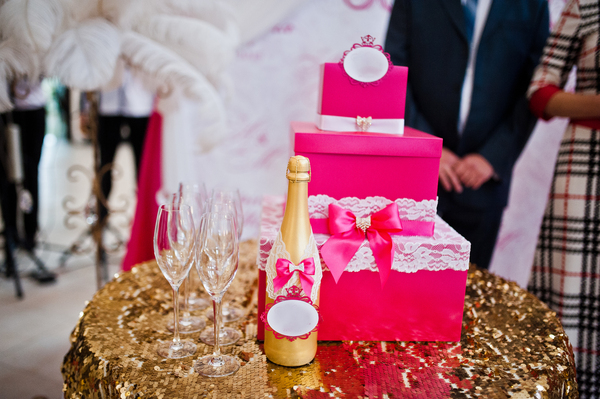 Geldgeschenk Hochzeit basteln: Kreative Ideen, die das Brautpaar lieben wird Hochzeitsgeschenke, Hochzeitsblog Pinker Geschenkbox-Turm mit Spitzen-Deko und goldene Sektflasche auf dem Gabentisch.