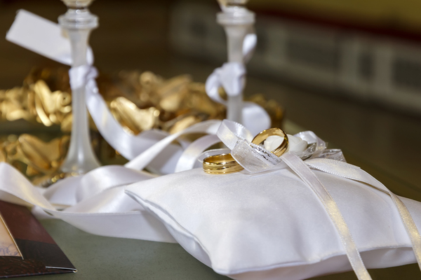 Goldene Hochzeit: Die schönsten Ideen, Wünsche und Sprüche zum 50. Ehejubiläum Hochzeitsjubiläen, Hochzeitsblog Zwei goldene Eheringe, die dekorativ auf einem weissen Satin Ringkissen mit Schleifen liegen.