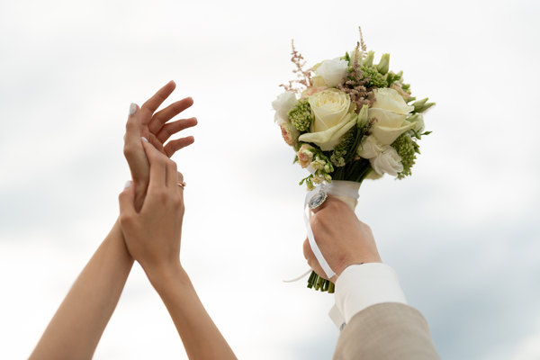 Persönliche Glückwünsche zur Hochzeit: So findest du die perfekten Worte Hochzeitswünsche, Hochzeitsblog Braut und Bräutigam strecken ihre Hände Richtung Himmel, wobei der Bräutigam einen Brautstrauss mit weissen Rosen hochhält.