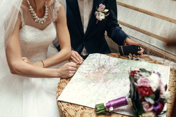 Brautpaar studiert gemeinsam eine Strassenkarte zur Routenplanung, daneben der Brautstrauss.
