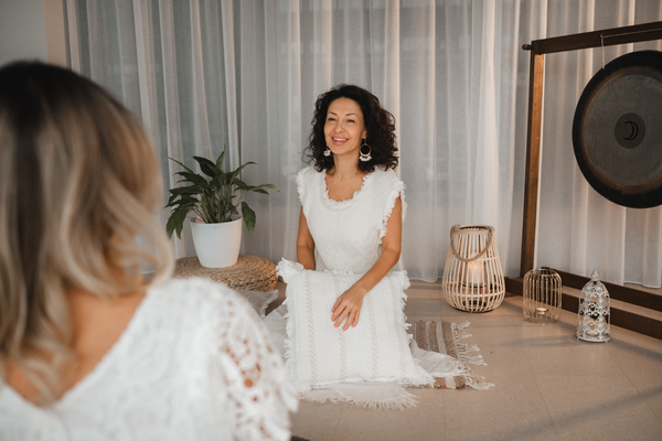 Perlenhochzeit: Alles über den 30. Hochzeitstag, seine Bräuche und Bedeutung Hochzeitsjubiläen, Hochzeitsblog Lächelnde Frau in Weiss bei einer Klangmeditation mit Gong im Hintergrund.