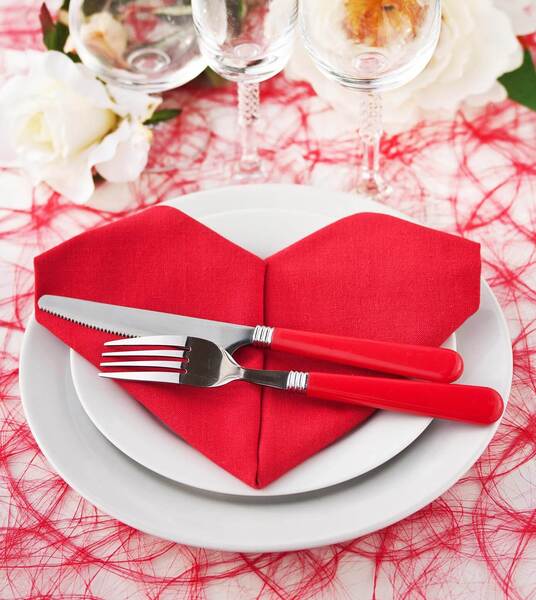 Servietten falten Hochzeit: Der ultimative Guide mit 11 zauberhaften Faltanleitungen DIY Hochzeit, Hochzeitsblog Eine rote Stoffserviette, die kunstvoll zu einem Herz gefaltet wurde und mit Besteck belegt ist – eine romantische Idee für das Servietten falten zur Hochzeit.