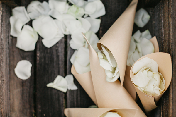 Spitztüten aus Papier, gefüllt mit weissen Blütenblättern, liegen bereit für die Gäste – eine klassische und schöne Idee für die Feier einer Papierhochzeit.