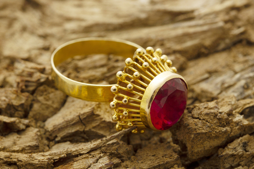 Rubinhochzeit: Der ultimative Guide für einen unvergesslichen 40. Hochzeitstag Hochzeitsjubiläen, Hochzeitsblog Goldener Ring mit grossem roten Edelstein liegt auf rauer Baumrinde; der Fokus liegt auf dem funkelnden Stein.