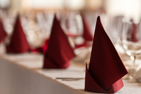 Zwei rote Servietten, die zu einer einfachen Pyramide gefaltet sind, eine klassische stehende Faltanleitung für die Tischdeko einer Hochzeit.