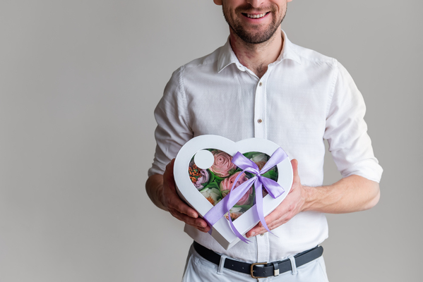 Geschenk für Ehemann: Der ultimative Guide mit 101 unvergesslichen Ideen Hochzeitsgeschenke, Hochzeitsblog Mann im weissen Hemd hält eine herzförmige Geschenkbox mit lila Schleife