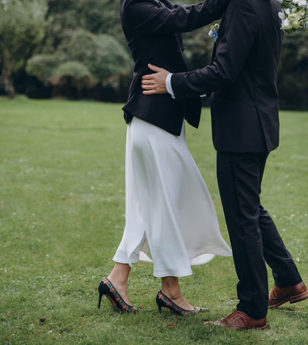 Gästebucheintrag Hochzeit: Der ultimative Guide für unvergessliche Glückwünsche Hochzeitswünsche, Hochzeitsblog Ein festlich gekleidetes Paar auf einer Wiese; sie umarmen sich oder tanzen, sichtbar sind Kleidung und Beine.