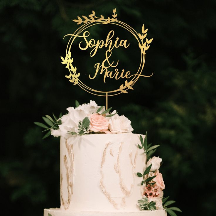 Cake Topper Hochzeit personalisiert: So gestaltest du deine Torte mit eurer Liebesgeschichte Hochzeitsplanung, Hochzeitsblog Ein filigraner, goldener Cake Topper Hochzeit personalisiert mit den Namen „Sophia & Marie“ in einem Blätterkranz auf einem eleganten Hochzeit Cake.
