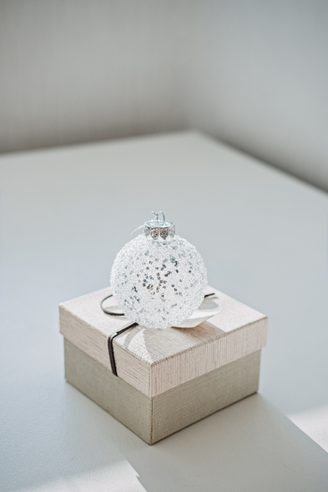 Gnadenhochzeit: Dein unvergesslicher Guide für den 70. Hochzeitstag Hochzeitsjubiläen, Hochzeitsblog Weisse Glaskugel mit Glitzer liegt auf einer beigefarbenen Geschenkbox mit Band auf einem hellen Tisch