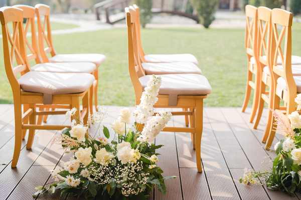 Sitzordnung Hochzeit: Der ultimative Guide für eine harmonische und unvergessliche Feier Guides, Hochzeitsblog Detailansicht einer eleganten Sitzordnung für die Hochzeit, bei der Holzstühle mit Blumenschmuck den Weg zum Altar säumen.